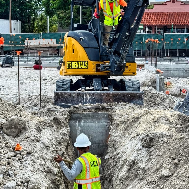 man in a ditch with an excavator digging in front of him